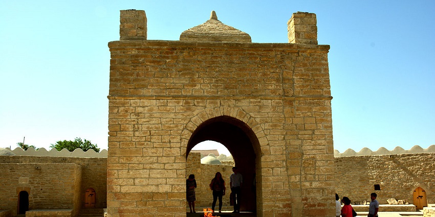 Ancient Zoroastrian fire temple with a central altar surrounded by stone chambers under an open sky.