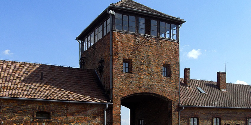 Brick entrance gate with watchtower at Auschwitz II-Birkenau under blue sky with sunlight, one of the historical places in Europe.