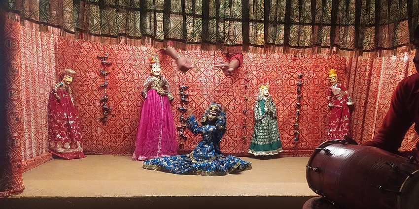 On-going puppet show with different unique puppets and a person holding a hand drum.