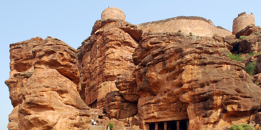 Rock-cut cave temples in rugged cliffs, with tourists exploring the ancient architecture.