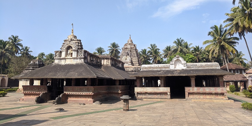 An ancient stone temple with carved pillars, surrounded by coconut trees, amongst the best places to visit in Karnataka in November.