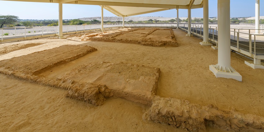 Ruins in the sand made up of small black stones and small hills at a distance.