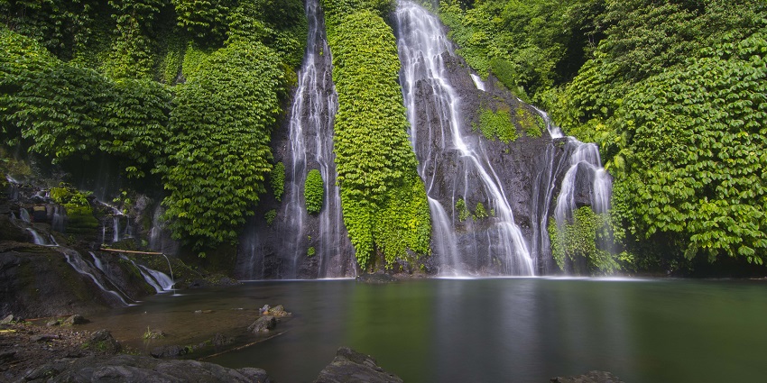 Banyumala twin waterfalls with the water flowing on the rocky surface into a lake.