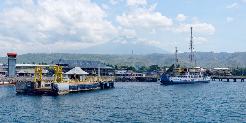 The ferry docked at a coastal port with calm blue waters and hills under a bright sunny sky.