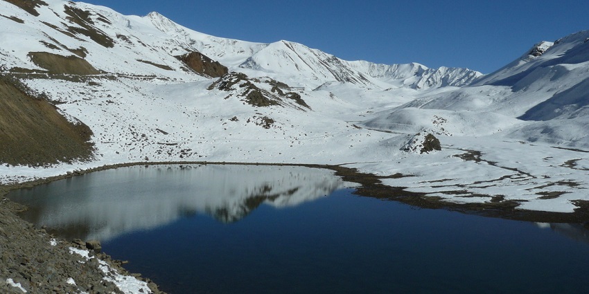 Green mountains with snowy mountains back and clear river water at the green valley.