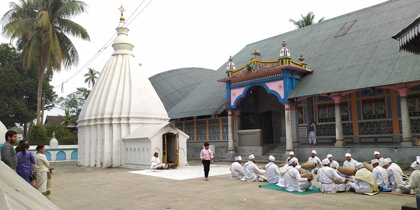 Barpeta Satra with people in white dresses, sitting and holding musical instruments, one of the places to visit in Assam in May.