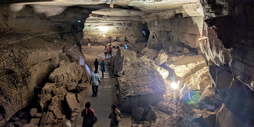 Tourists walk through a large, illuminated underground cave with rugged rock formations, one of the best places to visit in Andhra Pradesh in March.