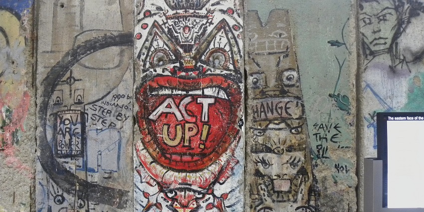 Berlin wall with unique red, black & blue graffiti on the wall and a screen on the right side