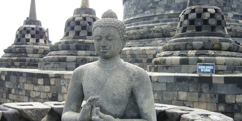 A stone Buddha statue sits in a meditative pose amid carved stupas at the Borobudur Temple, one of the famous monuments in Indonesia.