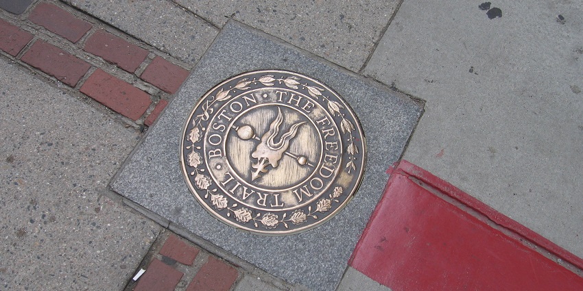Bronze Freedom Trail marker set at Boston sidewalk in red brick and paint trail.