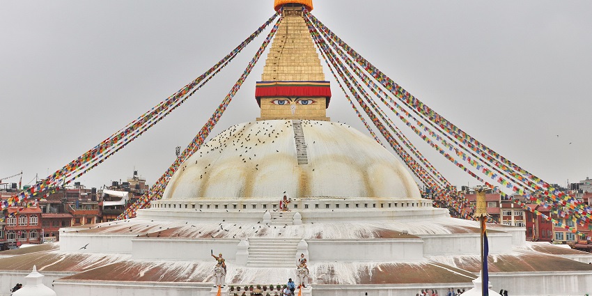 View of Boudhanath Stupa with colourful prayer flags and devotees circling the sacred site.