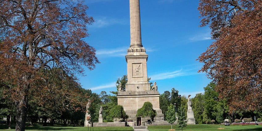 A tall stone column of Brock’s Monument with a statue surrounded by autumn trees, Canada