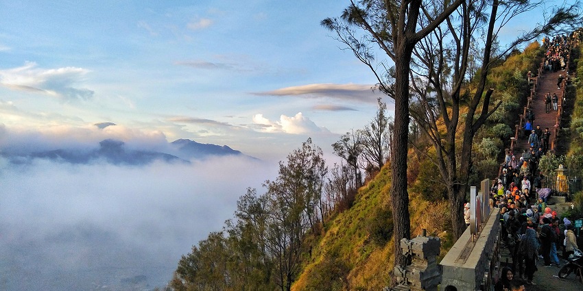 Bukit Cinta viewpoint with distant Mount Penanjakan covered in clouds and sun rising.