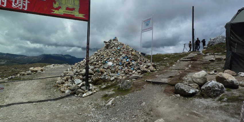 Bumla pass with piled-up small rocks, multiple sign boards and distant people standing
