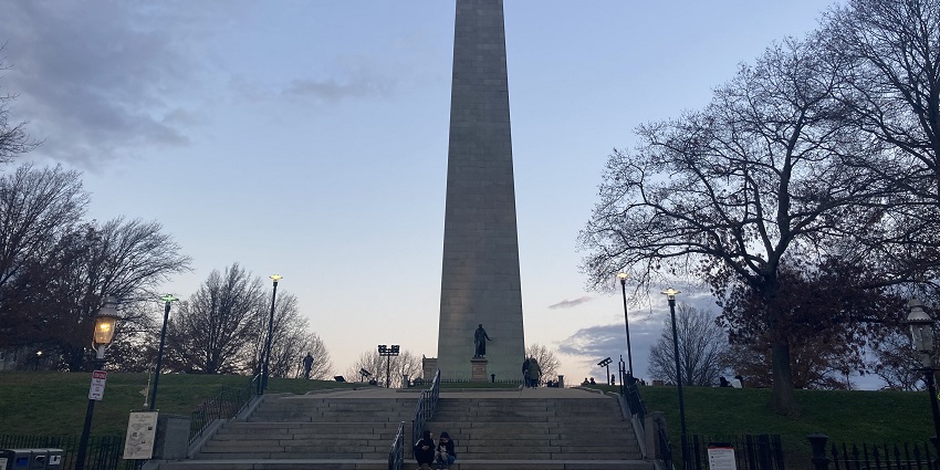 The Bunker Hill Monument stands tall at dusk with trees and stairs in the foreground.