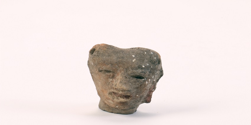 Small heart-shaped earless head figurine made out of clay against a light background