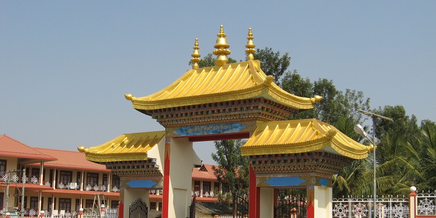 Golden Tibetan monastery with two monks against a brilliant blue sky with trees in the background.