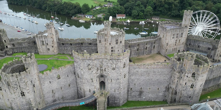 Caernarfon castle from above with old architecture, stairs leading to the castle and Ferris wheel.