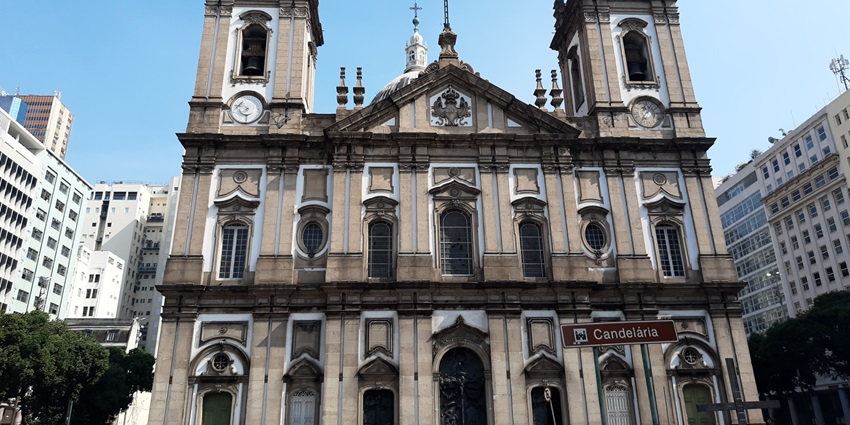 Baroque-style church facade with twin bell towers and ornate, surrounded by buildings