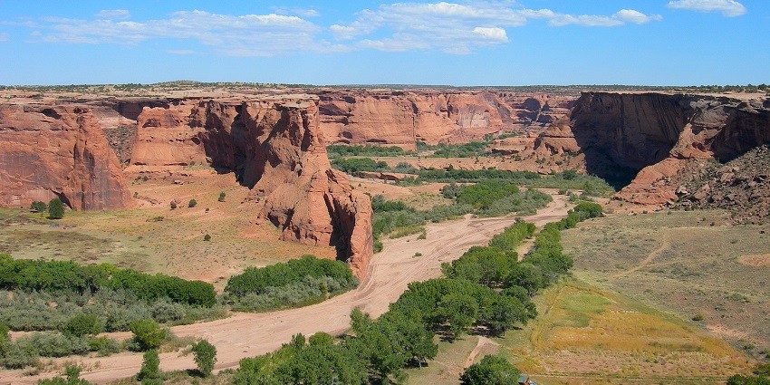 Expansive view of Canyon de Chelly with red rock cliffs, greens, and winding canyon floor.