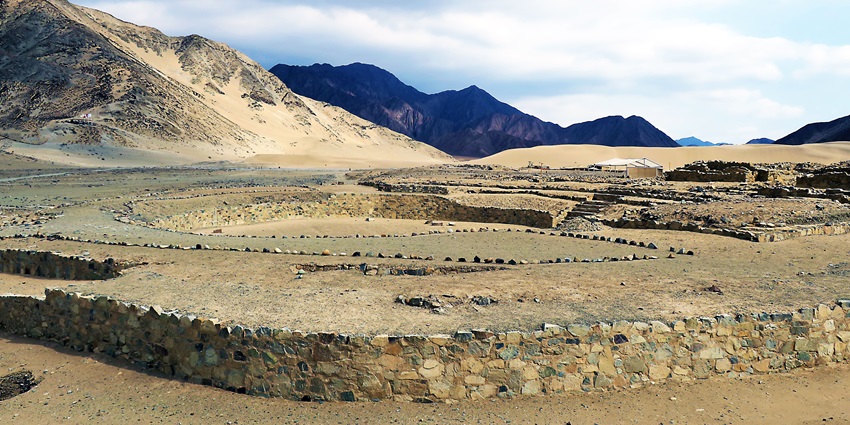 Ancient stone ruins across a dry, sandy landscape, one of the popular monuments in Peru
