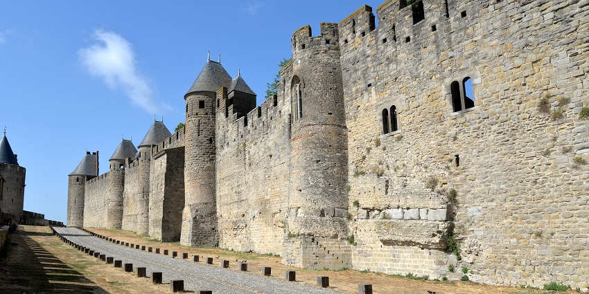 Medieval stone fortress with towers and crenellated walls under a clear blue sky.