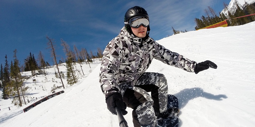 A skier dressed in winter gear skis down a snowy slope, surrounded by white snow and clear blue sky.