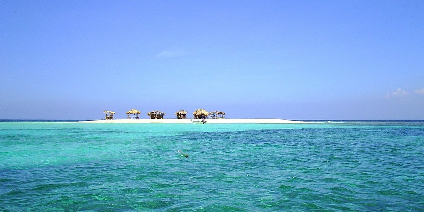 View of a secluded sandbar with thatched huts surrounded by crystal-clear turquoise waters.