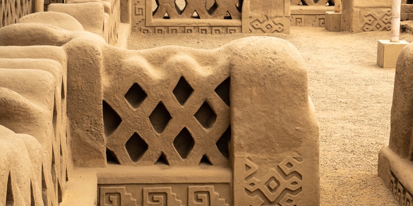 Intricately carved adobe walls with geometric patterns at Chan Chan monuments in Peru.