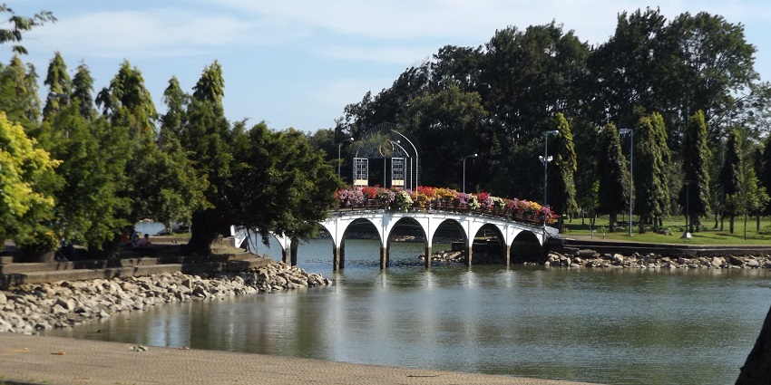 City park in Chanthaburi with a distant white architectural bridge and green trees, is one of the most beautiful places to visit in Thailand in July.