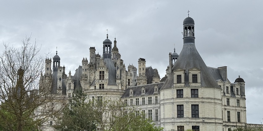 Ornate Renaissance-style castle with tall spires, seen from a garden under cloudy skies, one of the most beautiful historical places in France.