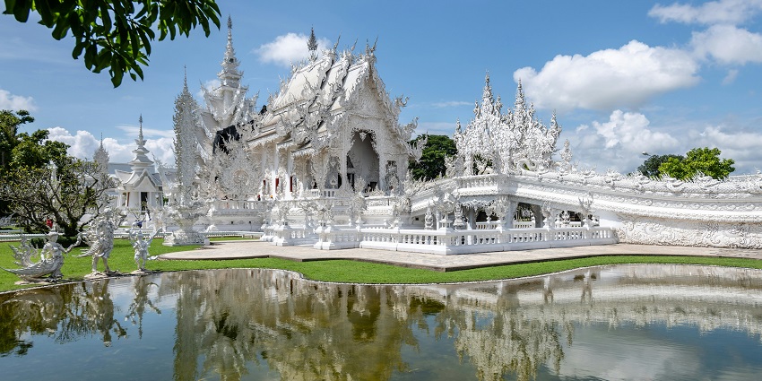 The white temple with detailed carvings and its architecture reflected in the lake is one of the top places to visit in Thailand in July.