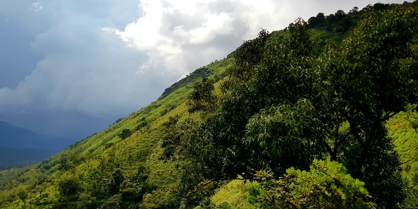 Valleys are wrapped in morning mist under a cloudy sky with lush green mountains, one of the places to visit in Karnataka in February.