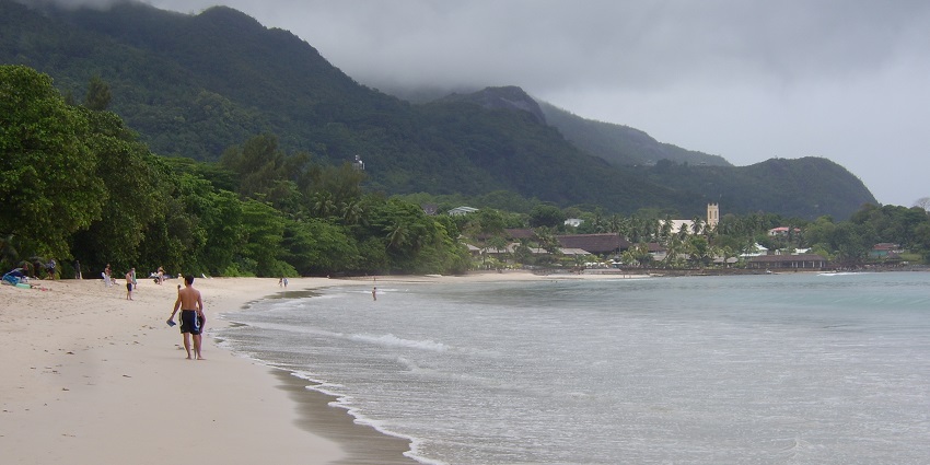 A stretch of sand with turquoise waves gently lapping the shore, surrounded by green hills.