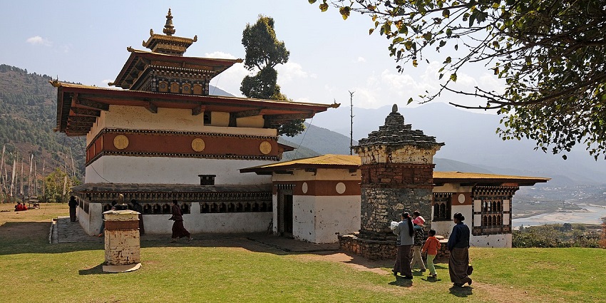 Chimi Lhakhang with traditional Buddhist architecture, people visiting and a river in the back.