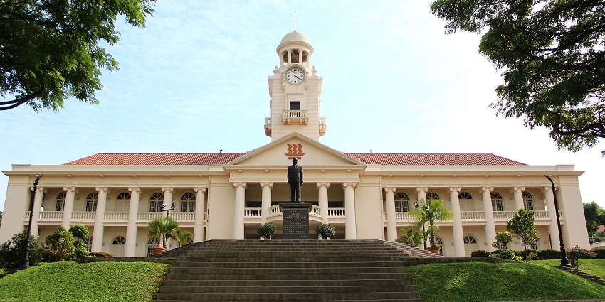 A grand colonial-style building with a clock tower and a statue in front, Singapore.