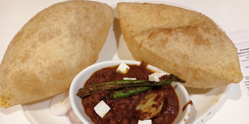 Fluffy deep-fried bhature served with spicy chickpea curry, pickles, and onions.