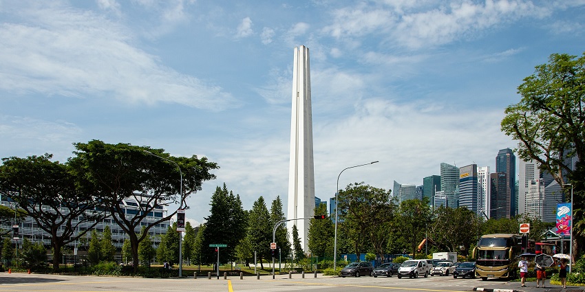 A tall, white obelisk-style structure in the cloudy sky, an iconic monument in Singapore.