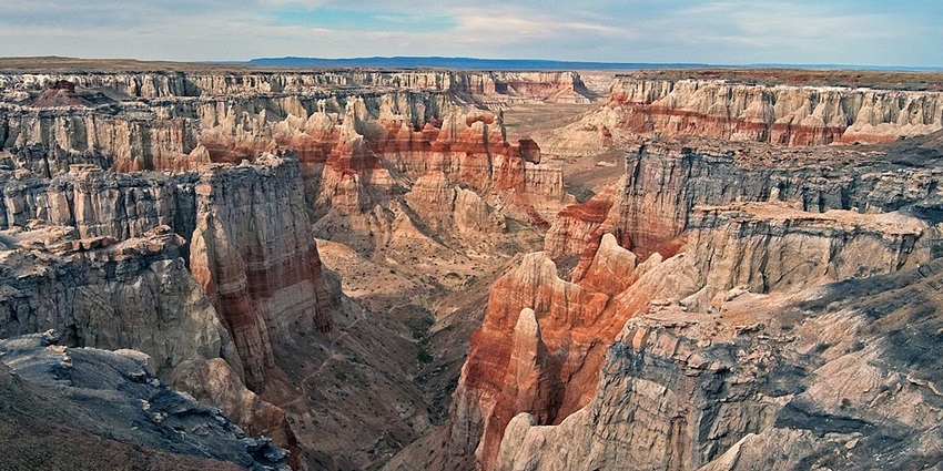 Coal mine canyon with rocky cliffs, orange sands, small grass bushes, and distant hills, one of the hidden places in Arizona.
