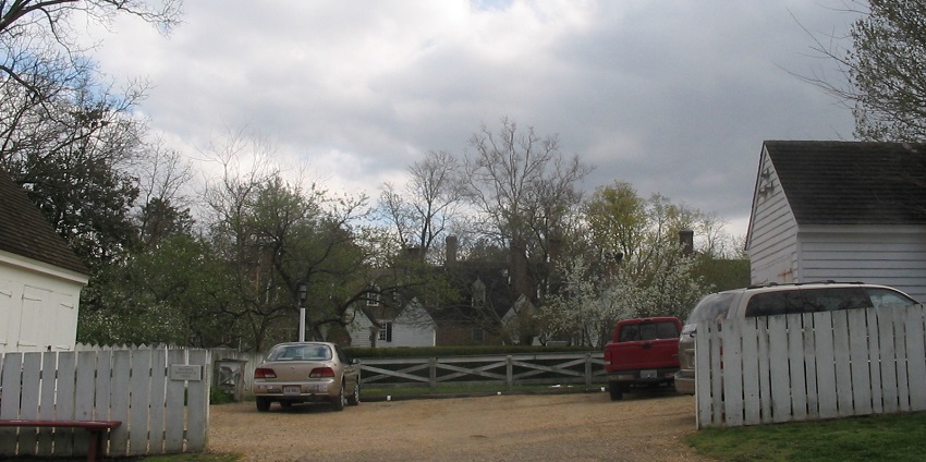 Country road with parked cars, white fences, trees, and cloudy sky in rural areas.