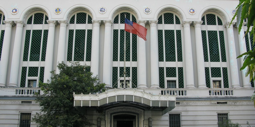 Old colonial-era building with faded white facade, wooden shutters, and arched doorways.