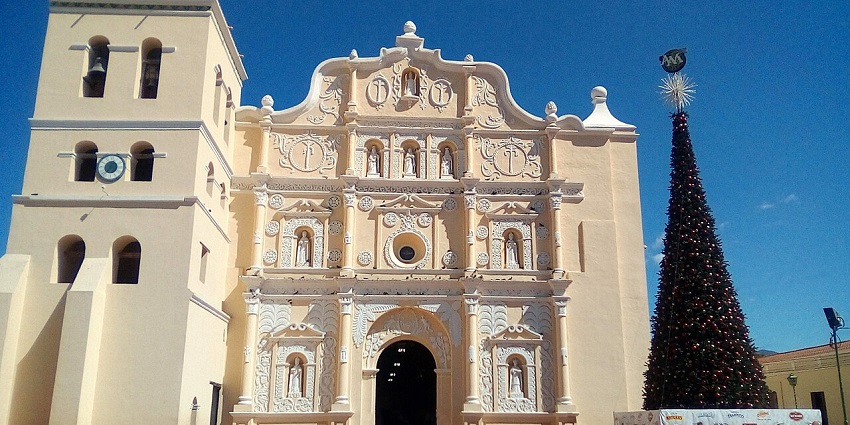 Stunning colonial-era cathedral with intricate architectural details stands beside a large decorated Christmas tree