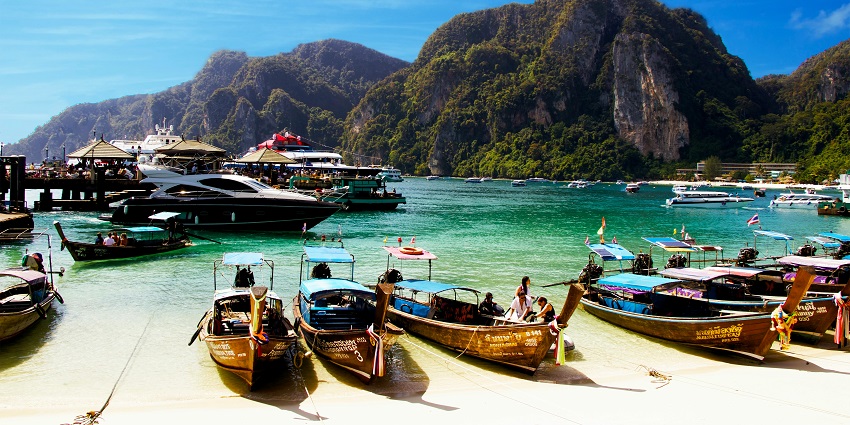 Wooden boat docked on white sand beach with clear blue sea and bright sky