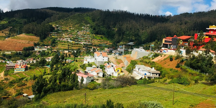 Panoramic view of town with colourful buildings nestled among lush hills and pine trees.
