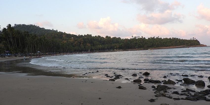 Corbyn’s Cove Beach with a rocky shore, visitors strolling, and a pinkish evening sky.
