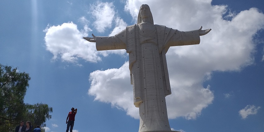 The Cristo de la Concordia statue towering under a blue, cloudy sky with visitors at the base.