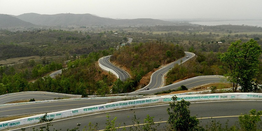 Motorcyclists navigate winding mountain roads lined with lush greenery and panoramic views.
