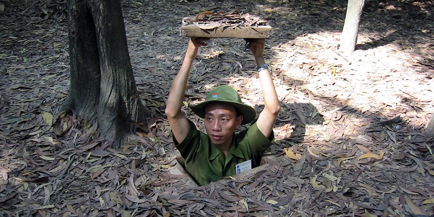 Demonstration of a concealed Cu Chi tunnel entrance with a soldier illustrating its use.