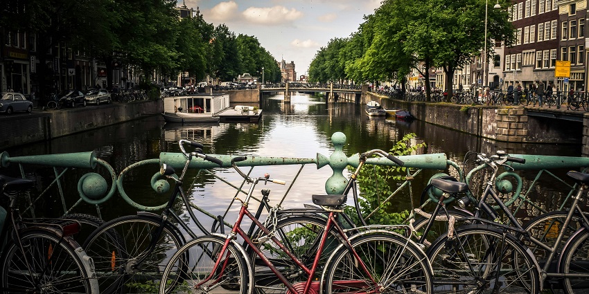Bicycles parked by blue rails near river, showing what Amsterdam is famous for