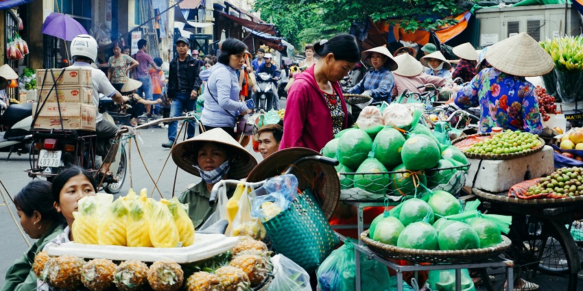 People walking through a busy open-air market during daytime with stalls on both sides